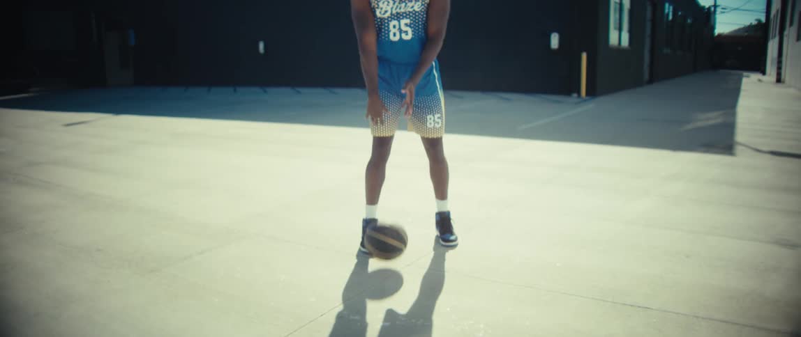 Basketball player holds the ball while standing on an outdoor court surrounded by industrial buildings