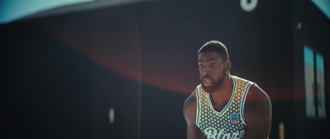 A black man with a beard wearing a blue and yellow basketball jersey with the number 85 is dribbling a basketball outdoors