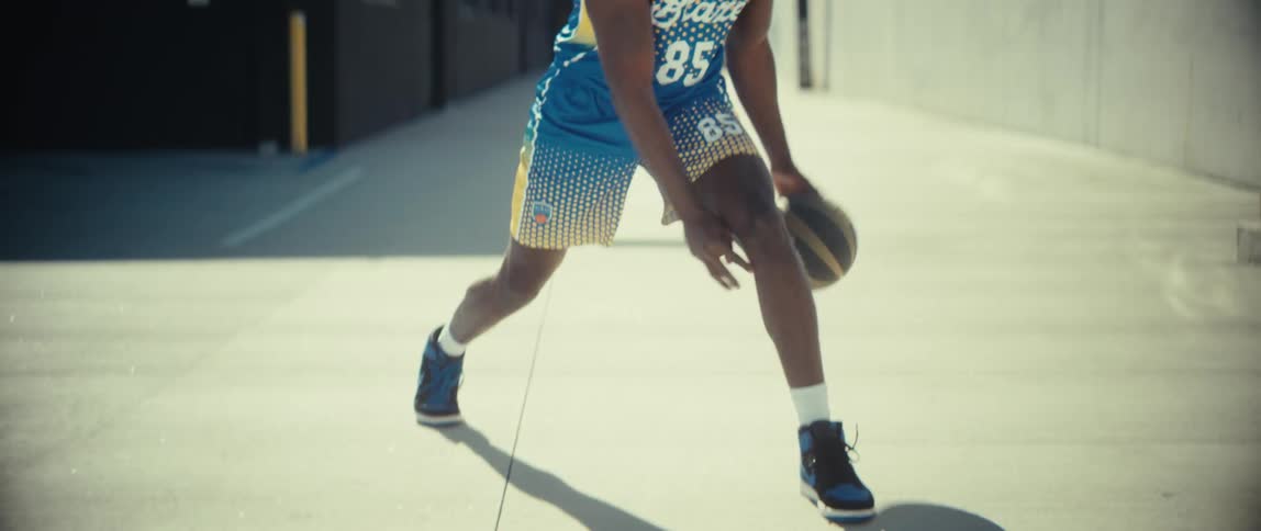 Person dribbles black and yellow ball on outdoor court under strong sunlight