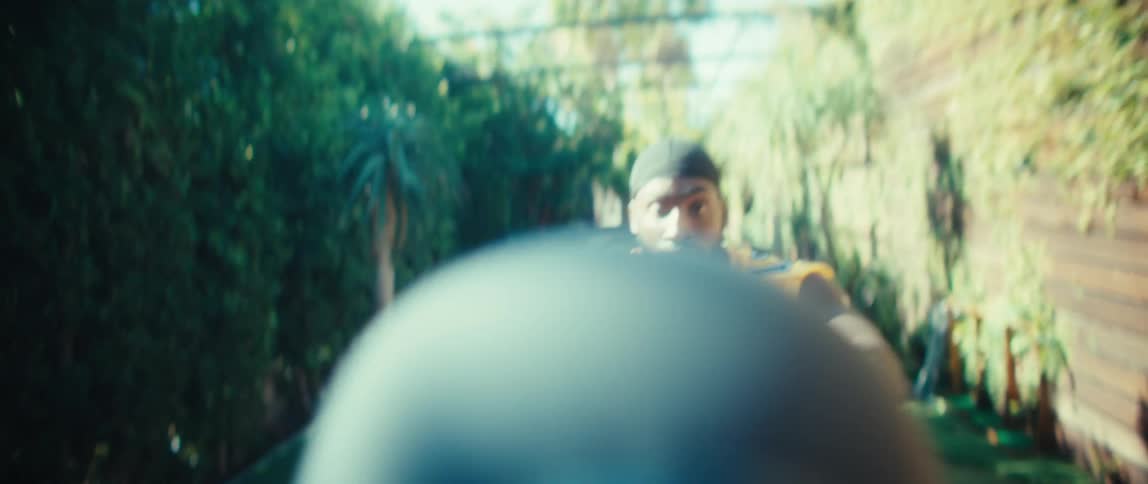 A black male athlete catches a spinning football while standing in an outdoor court during daytime