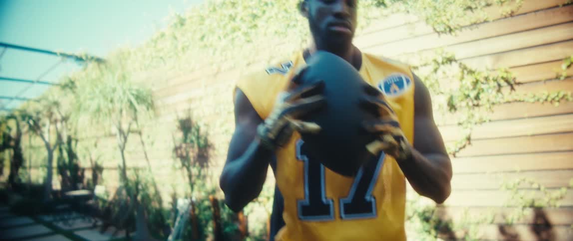 An american football player trains alone holding a football in a yellow jersey and throwing it back and forth with someone