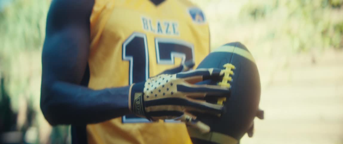 Close up of a young black male athlete appreciating a football while standing outdoors during daytime