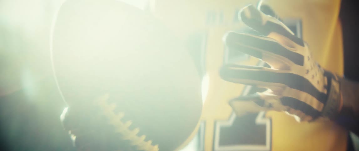 Player holding football with patterned gloves under intense light
