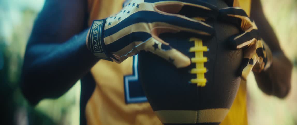 Person in yellow sports jersey holding football with black and yellow patterned gloves