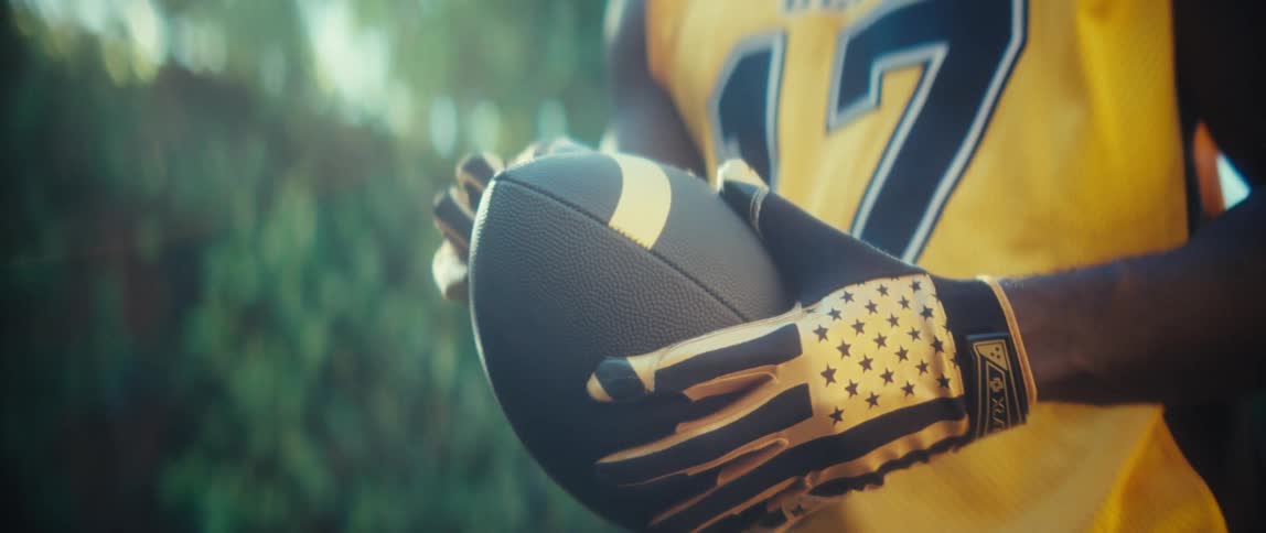 Close up of a black male athlete holding a football while standing outdoors during daytime