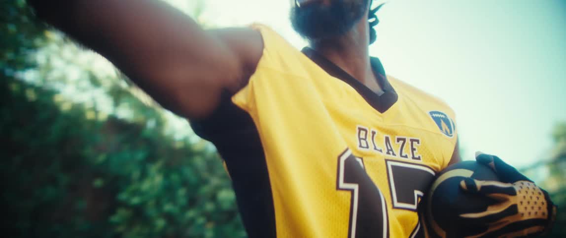 A young male black athlete catches a football while playing outdoors during daytime