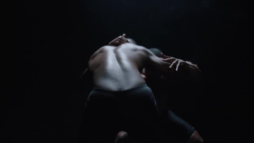 Two shirtless men fighting in an enclosed space with one of them knocking the other down