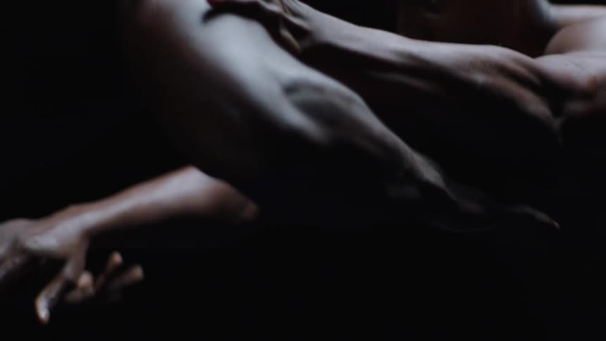 Two bare chested men wrestle in a dark area lit by a spotlight