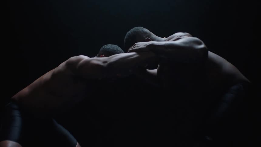 Two black men are wrestling in a darkened area