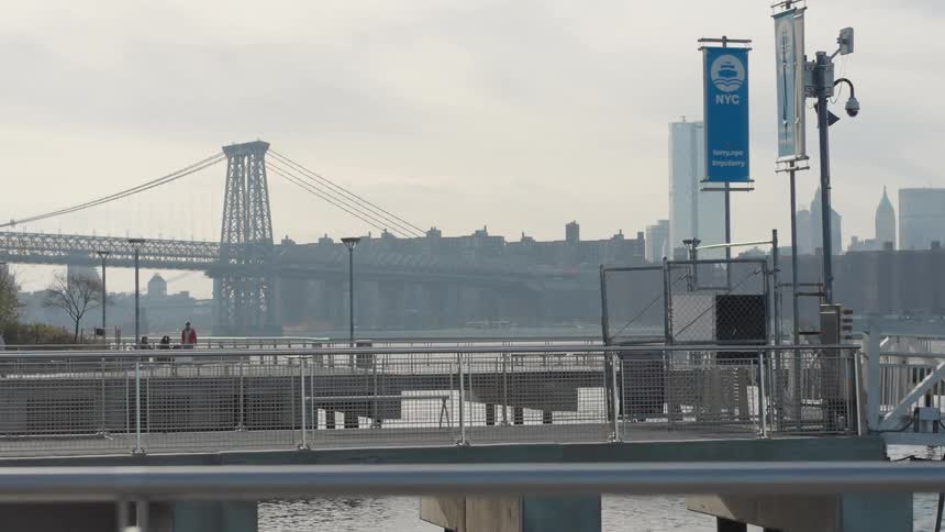 Metal bridge in the background viewed from an urban pier with railings poles and a new york city banner