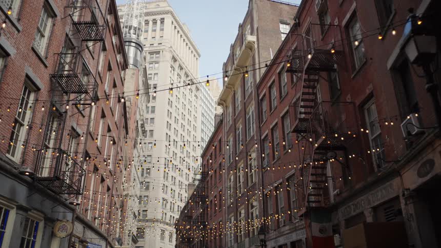 Narrow street between brick buildings with fire escapes and decorative string lights suspended overhead