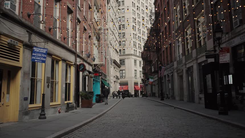 Cobblestone street between urban buildings with decorative string lights overhead and a few people walking