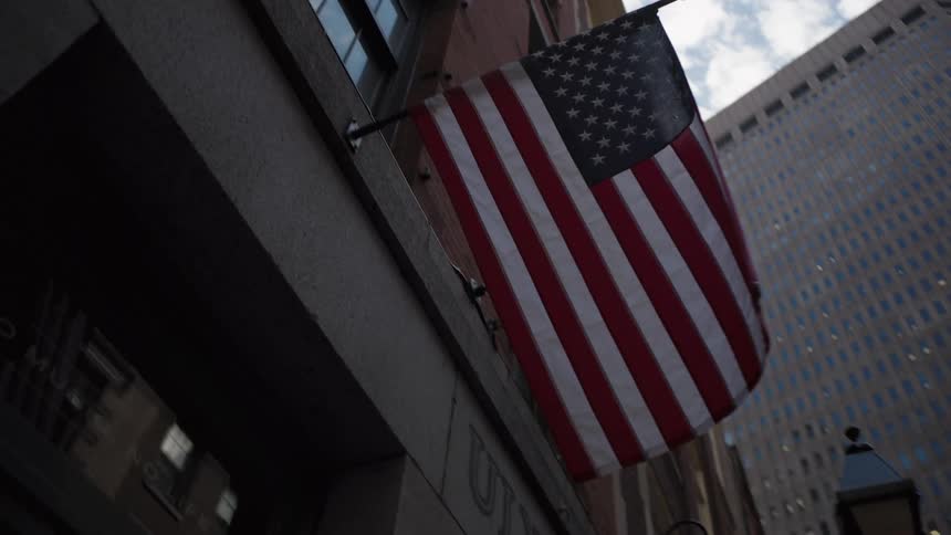 United states flag hanging on the facade of an urban building among tall buildings