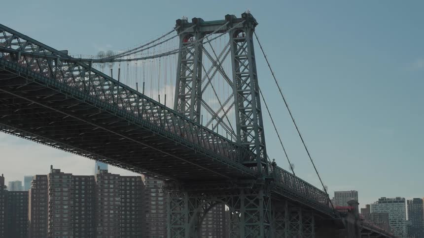 Williamsburg bridge spans the river with a suspended metal structure and residential buildings in the background