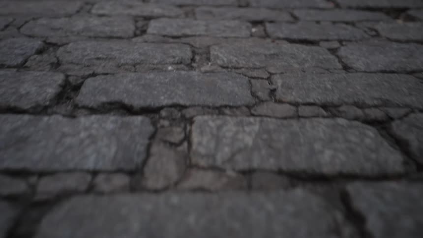 A slow steady backward movement across a worn cracked cobblestone street