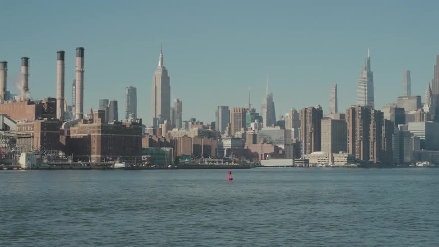 A calm waterfront view of a bustling city skyline with towering skyscrapers under a clear blue sky