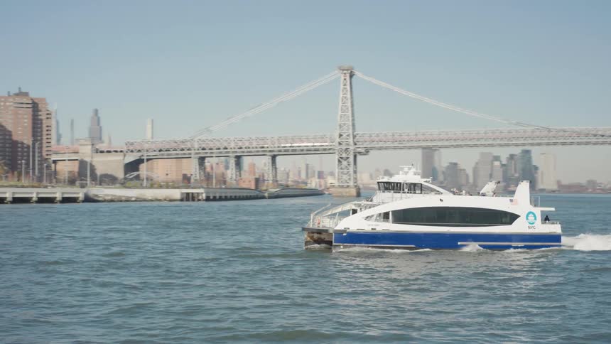 Boat sailing across the water off the metropolitan coast with a bridge in the distance
