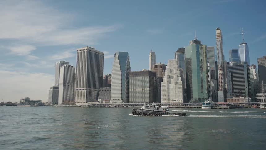 Two large watercraft move through the water leaving a wake while passing the downtown skyscrapers on a cloudy day