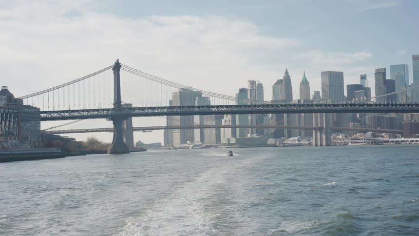 Boat sails under a bridge off the metropolitan coast with towers and buildings on the city skyline