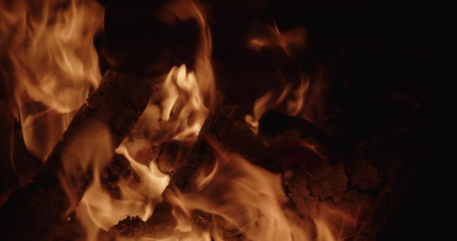 The flames of a campfire flicker and rise as the wood burns