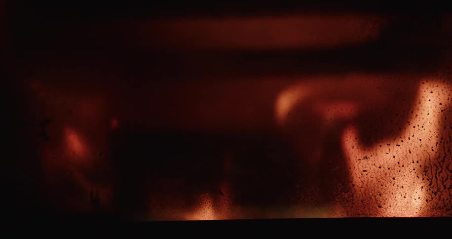 Warm gentle flames flicker inside a dark fireplace their soft glow seen through a sootcovered glass door