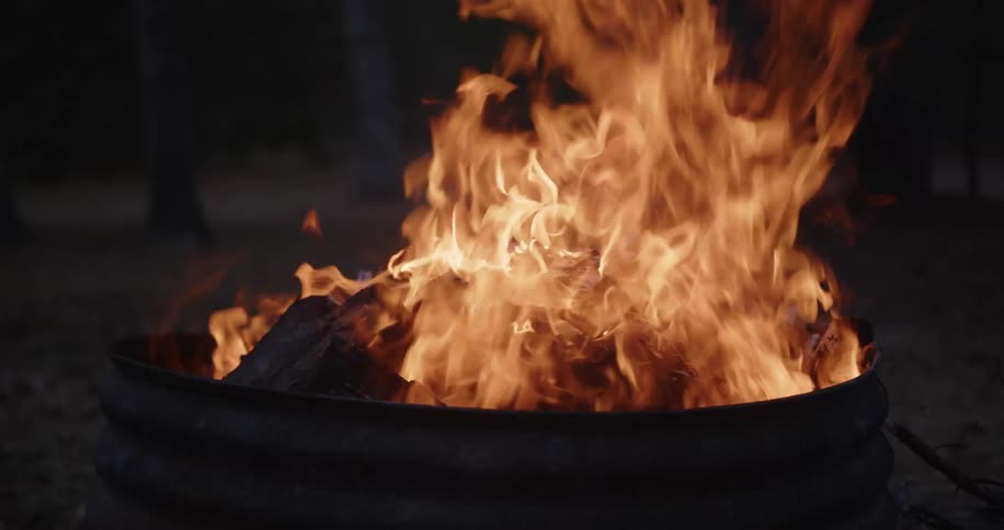 Fire burns intensely inside a metal container with pieces of wood in combustion