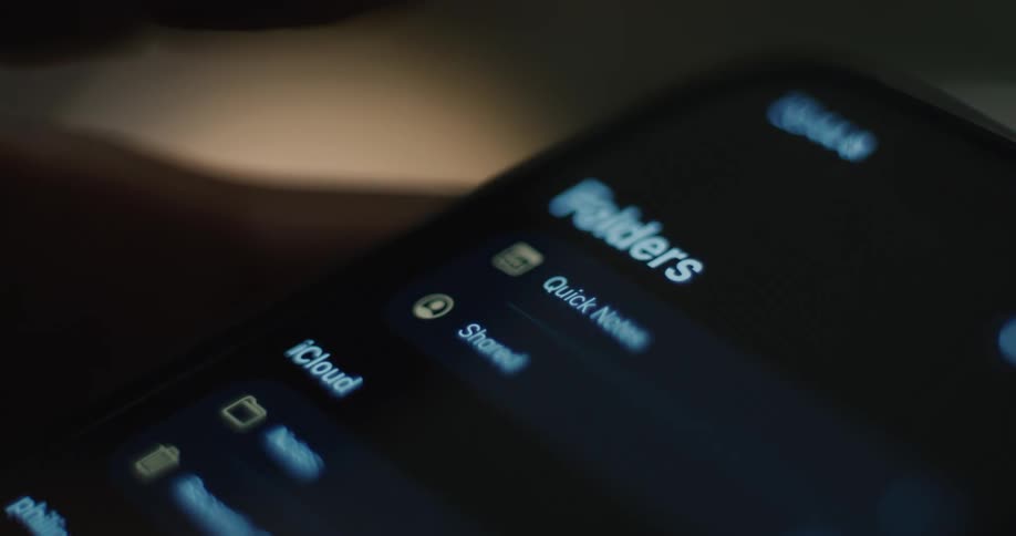 In a dimly lit setting a persons finger taps the notes app icon on a smartphone screen opening the application to its reminders app