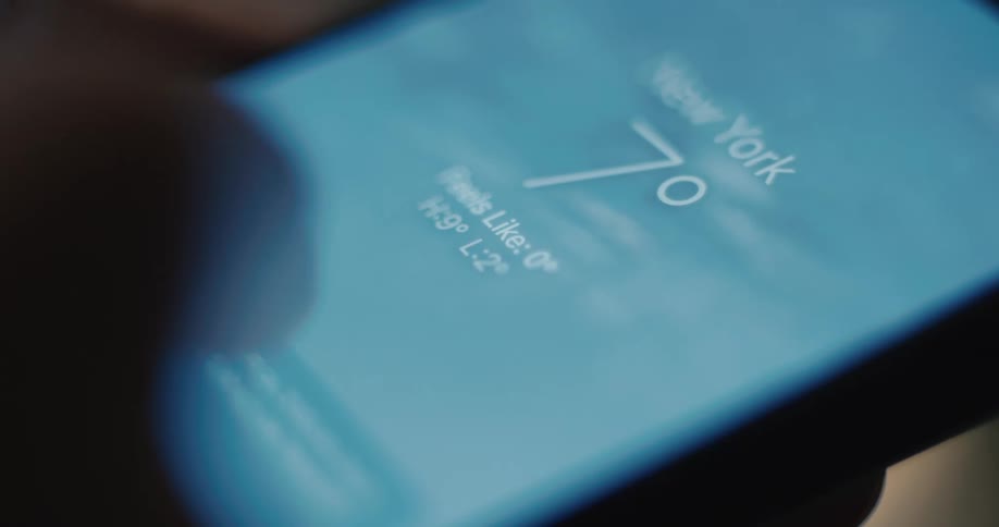 A mans finger taps an application on a dark smartphone screen then scrolls down through a summary of weather data indoors