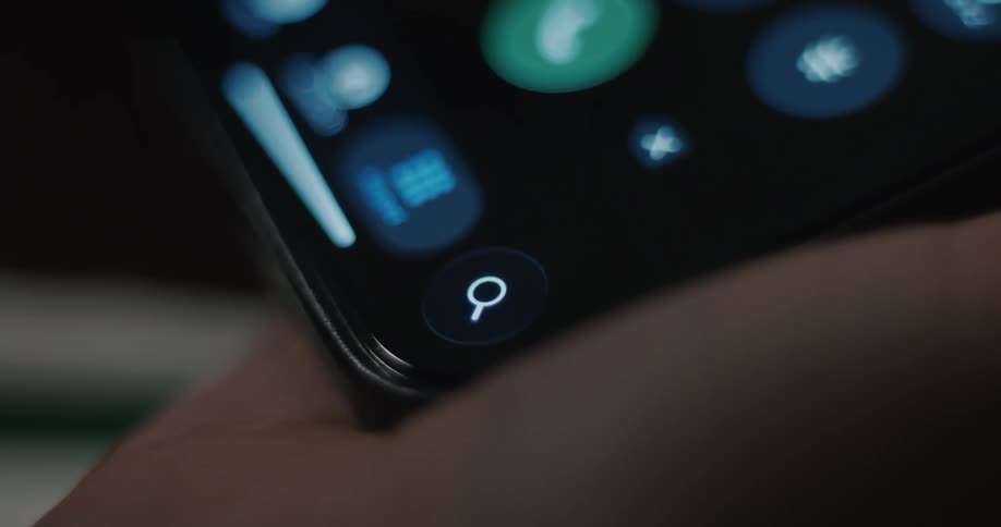 Closeup shot of a smartphone screen displaying app icons focusing primarily on the bottom row where a call icon and a search icon are visible as the phone is manipulated in a hand