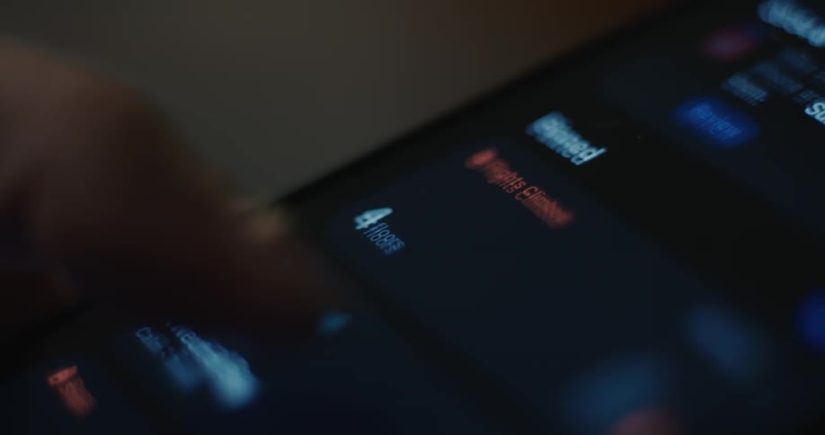 A close view shows a finger scrolling on a dark smartphone screen in a dim indoor setting