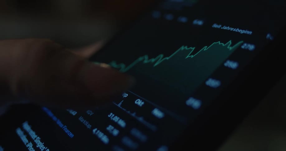 Finger touches a smartphone screen displaying a line financial chart on a dark interface