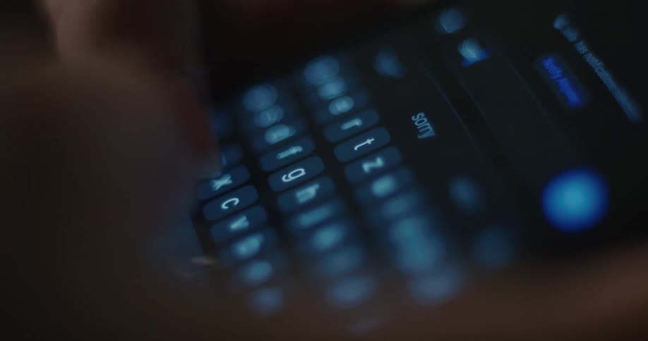 Person typing on an illuminated virtual keyboard on a smartphone screen