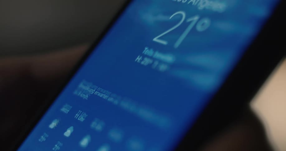 A close view shows a finger touching the weather application icon on a smartphone screen which opens to a blue screen displaying the forecast for new york
