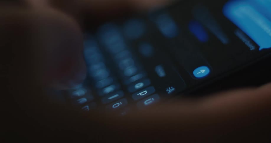 Finger presses an illuminated virtual keyboard on a smartphone screen while typing