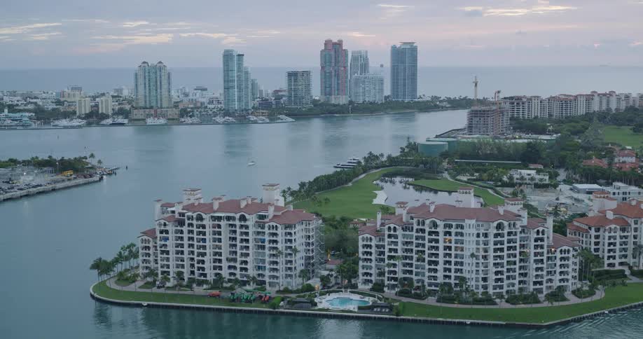 Apartment buidlings along the coast with towers in the distance with boats in a marina and sailing on the water