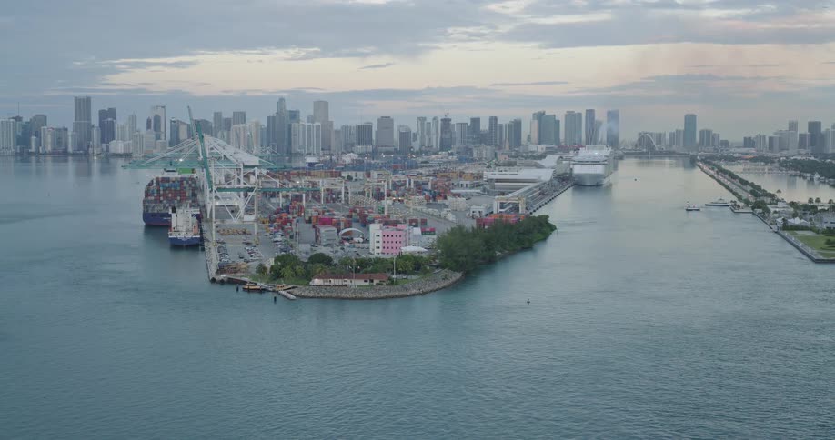 Seaport with cranes containers and ships occupies an artificial island in front of a waterfront urban skyline