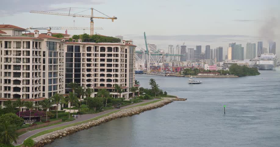 A city view by a seaport with a crane on the shoreline and a series of containers in the port at midday with the city skyline in the background