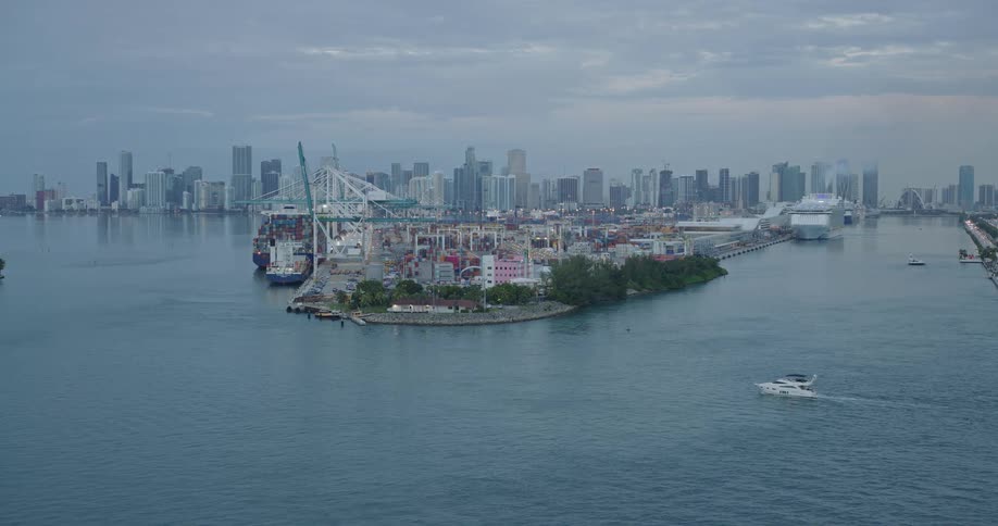 Aerial view of a busy container port with cargo ships and a city skyline in the background
