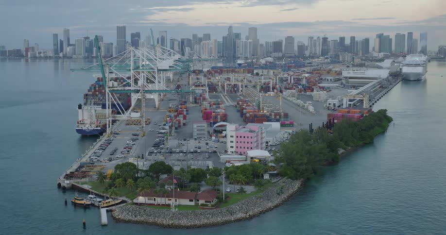 This video is an aerial shot of a large busy seaport with an extensive container terminal showcasing towering cranes and stacks of multicolored shipping containersin the background a dense urban skyline of modern skyscrapers rises across the water