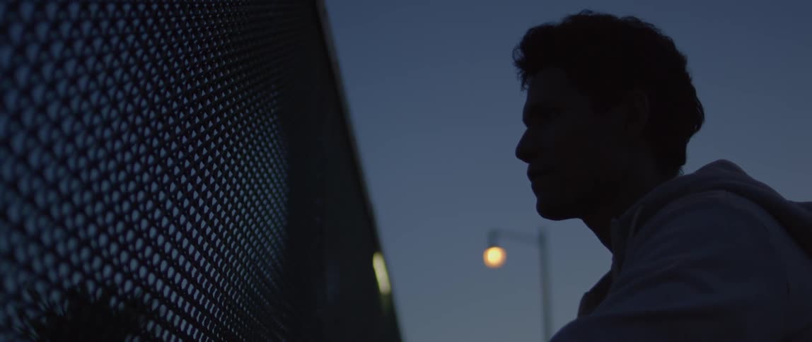 A man stands in front of a fence at dawn