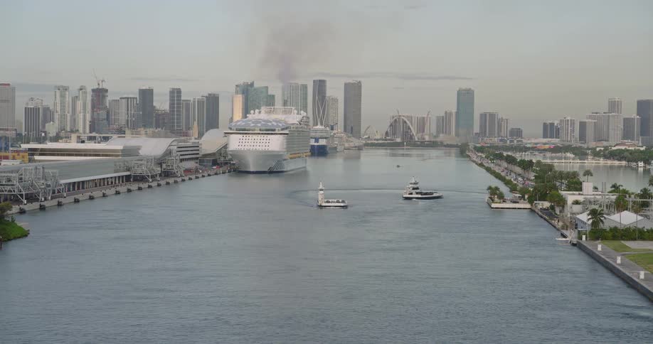 Yachts and boats float in a channel near a docked cruise ship as fog covers the skyline in the background