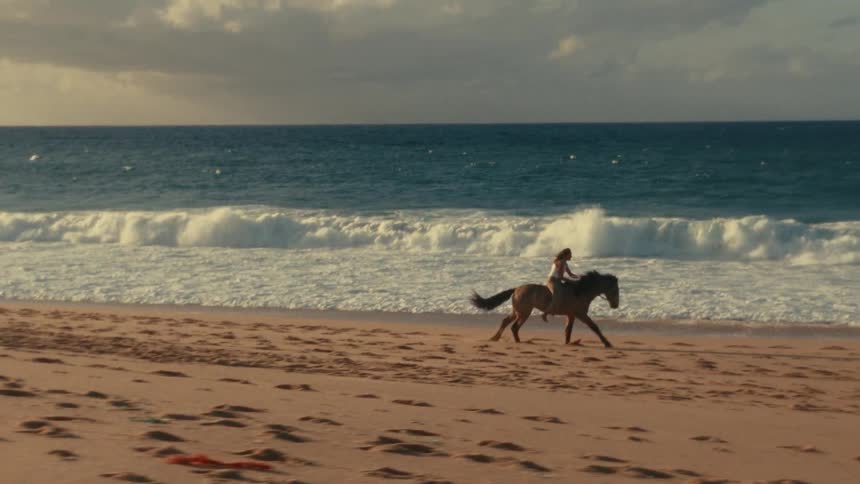 A person rides a horse along a sandy beach as waves crash by the ocean