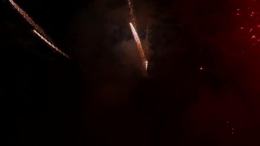 Colorful sparks from a fireworks display streak across a dark night sky with flashes of red gold and green light
