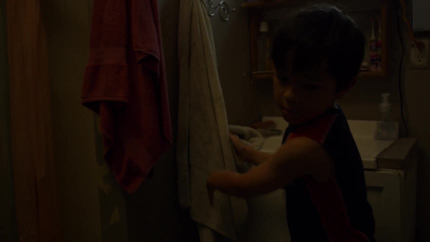 Boy washing and drying his hands in bathroom then walks out