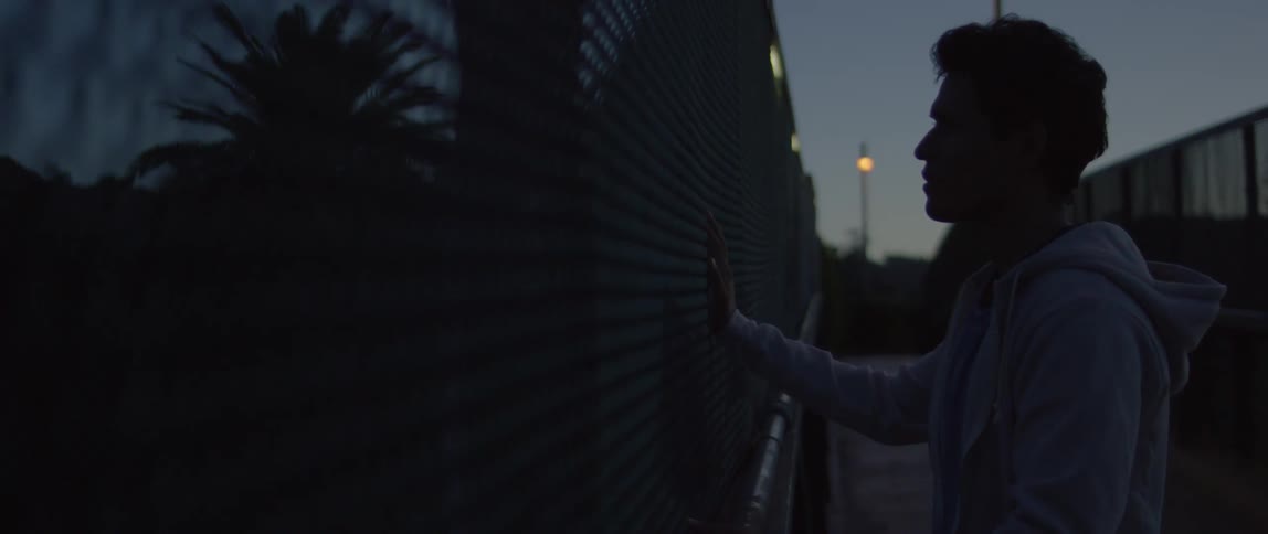 A man touches a chain link fence at night
