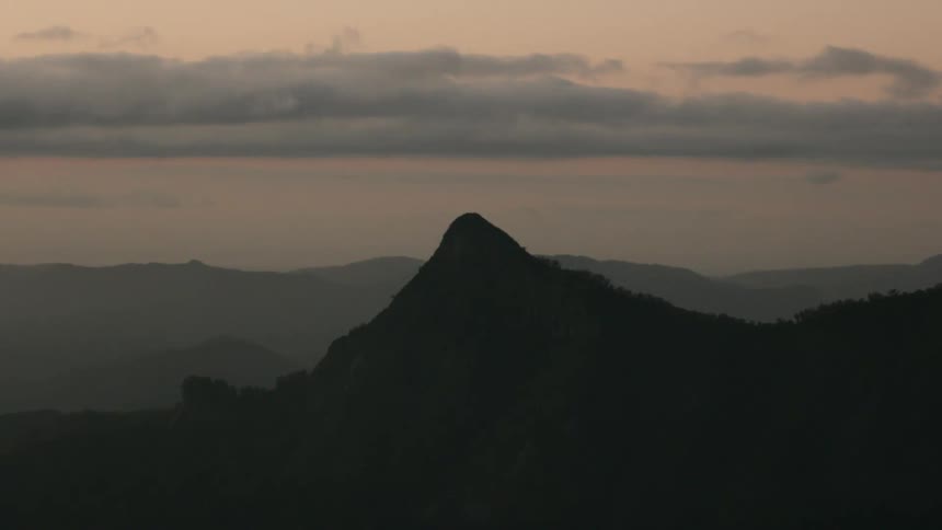 A dramatic distant view shows a sharply peaked dark mountain silhouetted against a cloudy twilight sky over rolling terrain