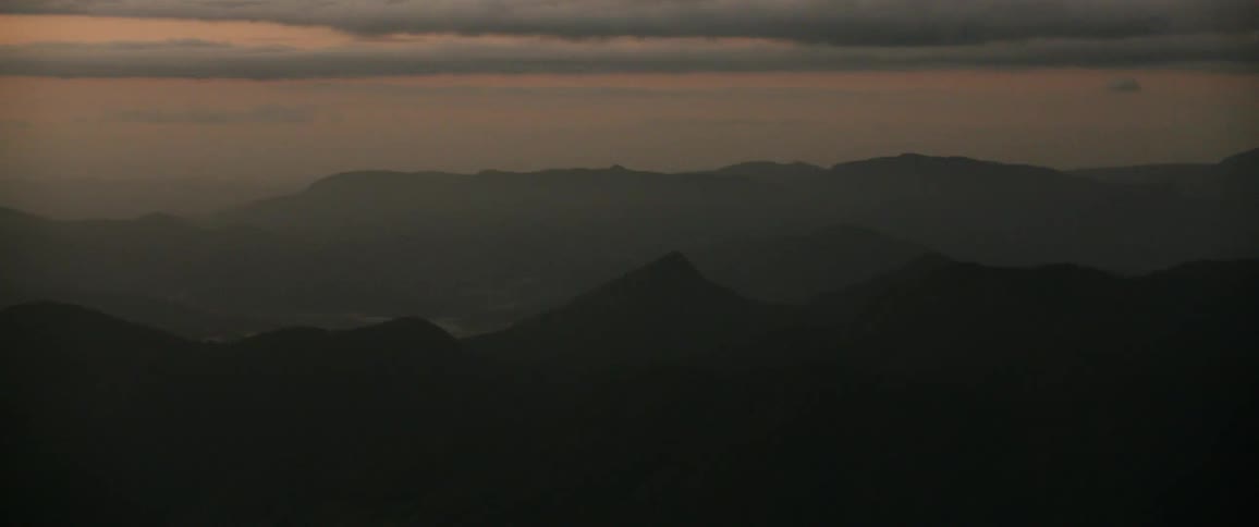 An ethereal vista of silhouetted mountain ridges fading into the distance is cast under a soft muted twilight sky