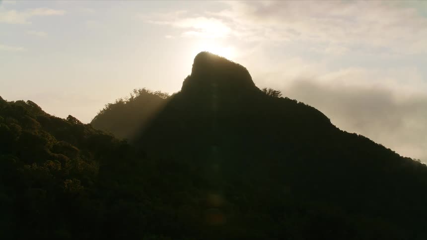 The peak of a silhouette mountain with sunlight in the background