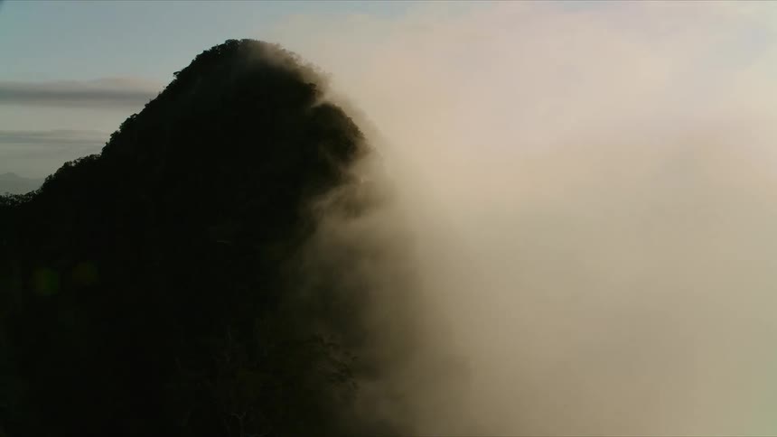 A dramatic mountain peak is partially obscured by a dense layer of lowhanging clouds and fog that blankets the landscape