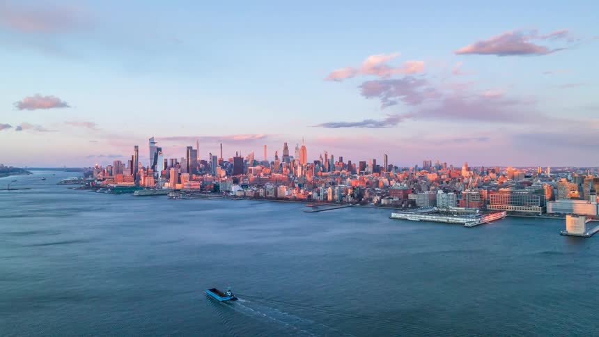 Urban skyline lit by late afternoon light stretches beyond a river with a boat in the foreground